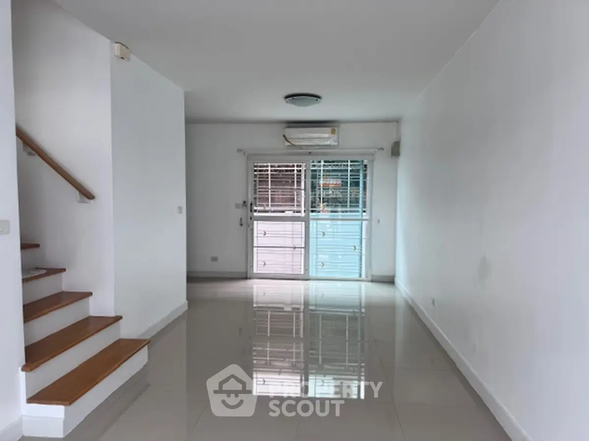 Spacious empty living room with glossy tiled floors and staircase, perfect for customization.