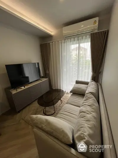 Modern living room with cozy sofa, large TV, and natural light from window.