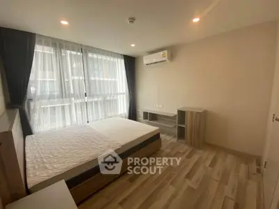 Modern bedroom with large window, wooden flooring, and air conditioning in a stylish apartment.