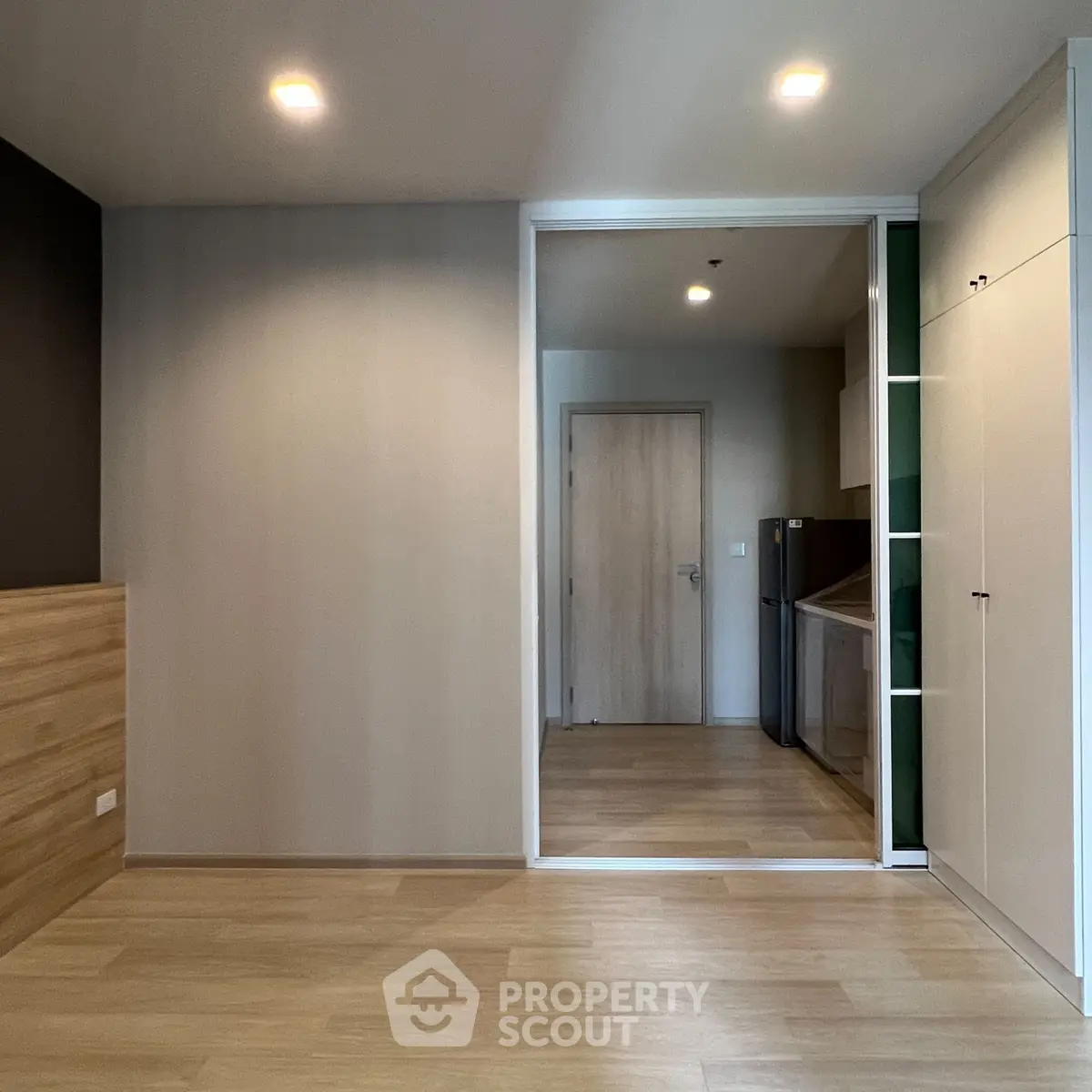 Modern apartment interior with wooden flooring and built-in storage, featuring a compact kitchen area.