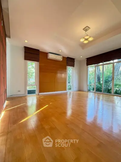 Spacious living room with wooden flooring and large windows offering garden views.