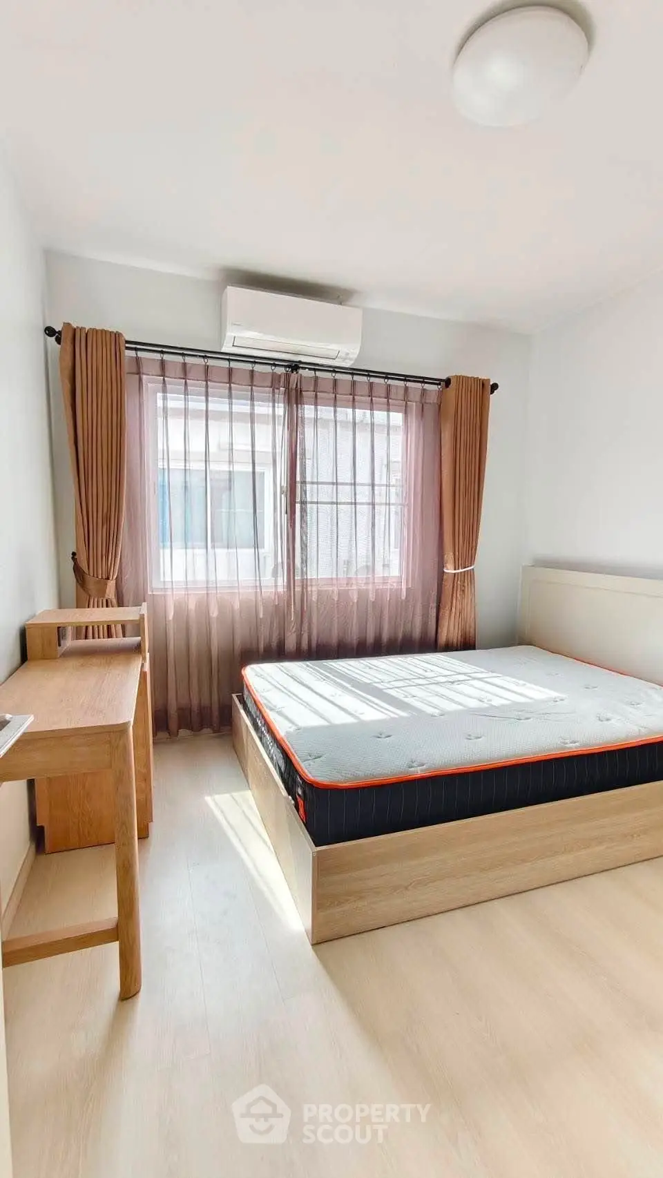 Bright bedroom with large window, wooden flooring, and modern furnishings in a cozy apartment.