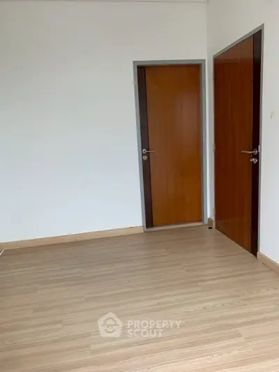Spacious empty room with wooden flooring and two wooden doors, perfect for customization.