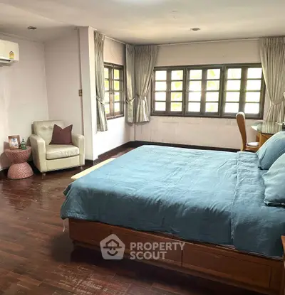 Spacious bedroom with wooden flooring and large windows for natural light