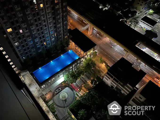 Stunning aerial view of illuminated rooftop pool in urban high-rise building at night.