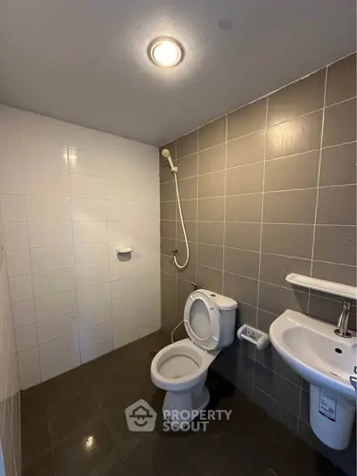 Modern bathroom with sleek gray tiles and white fixtures, featuring a shower and toilet.