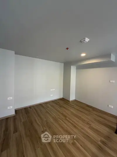 Spacious empty room with wooden flooring and modern lighting, perfect for customization.