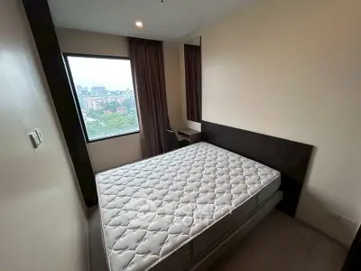 Cozy bedroom with large window offering cityscape views, featuring a comfortable mattress and minimalist decor.