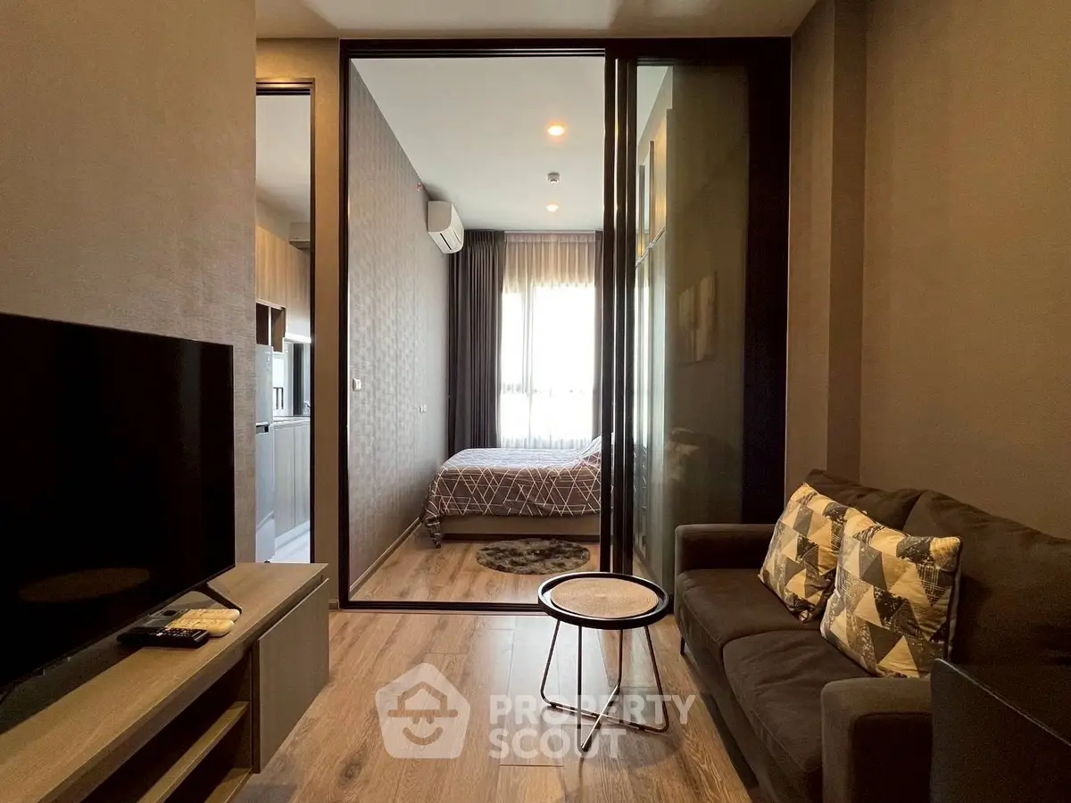 Modern apartment interior with cozy living room and stylish bedroom separated by glass partition.