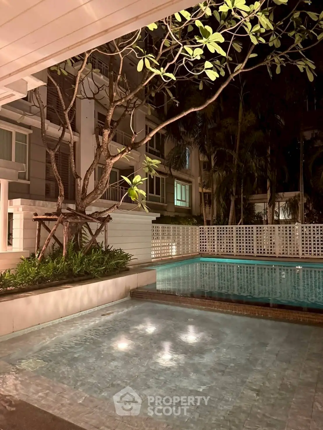 Luxurious night view of a serene residential pool surrounded by lush greenery and modern architecture.