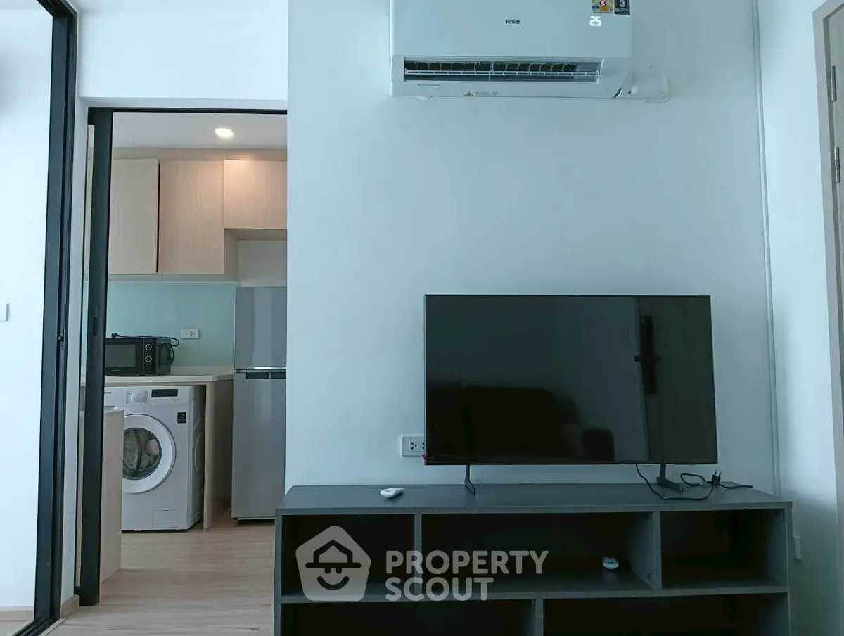 Modern apartment interior with TV, air conditioner, and kitchen appliances.