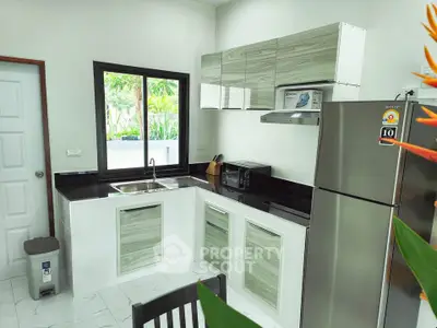 Modern kitchen with sleek cabinets and stainless steel appliances, featuring a large window and stylish decor.