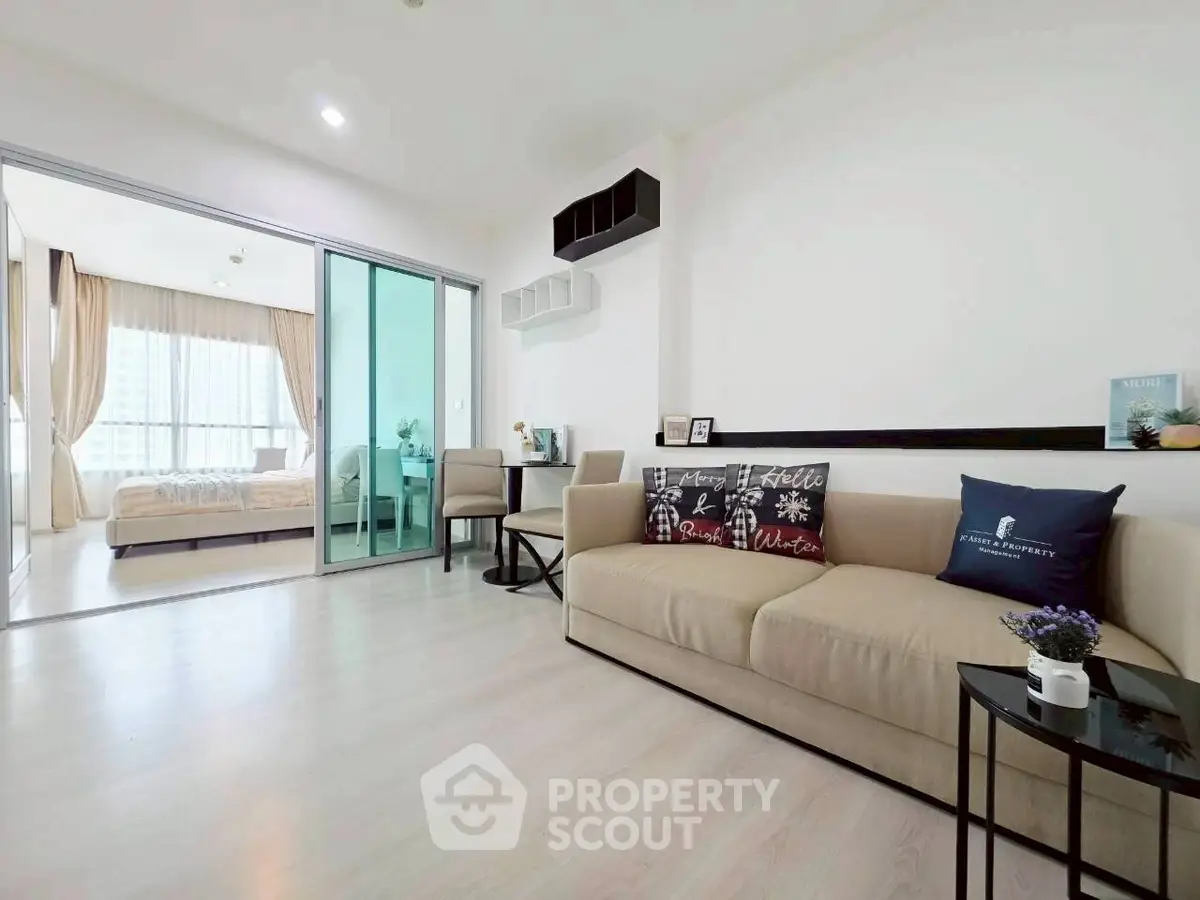 Modern living room with beige sofa and sliding glass doors leading to a bright bedroom.
