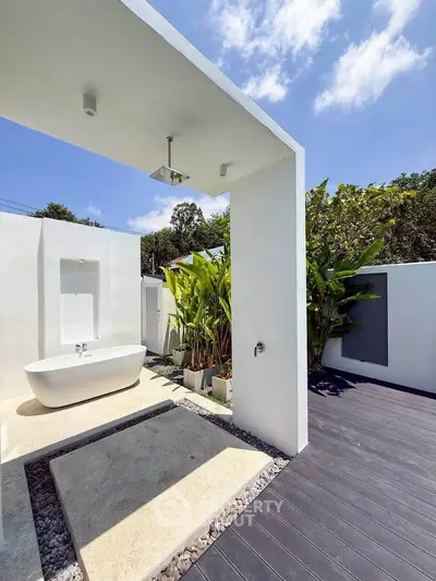 Luxurious outdoor bathroom with modern bathtub and lush greenery under a clear blue sky.