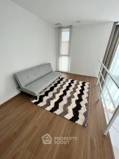 Minimalist living room with sleek grey sofa and stylish patterned rug, natural light from tall window, perfect for modern living.