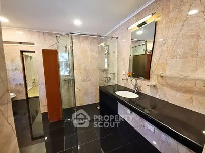 Luxurious bathroom with elegant marble walls and sleek black countertop, featuring a modern glass shower enclosure.