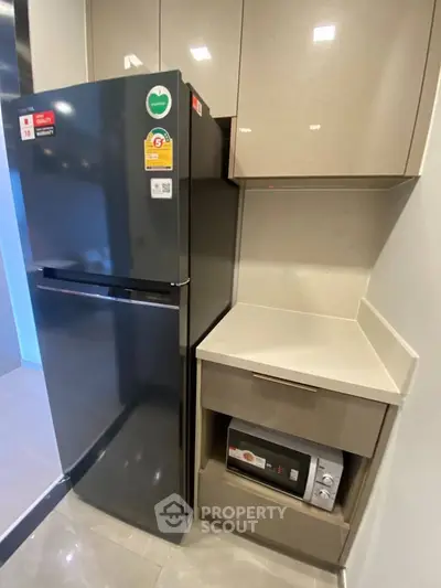 Modern kitchen corner with sleek fridge and built-in microwave in stylish cabinetry.