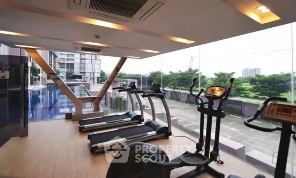 Modern gym with treadmills and exercise bikes overlooking a pool and cityscape.