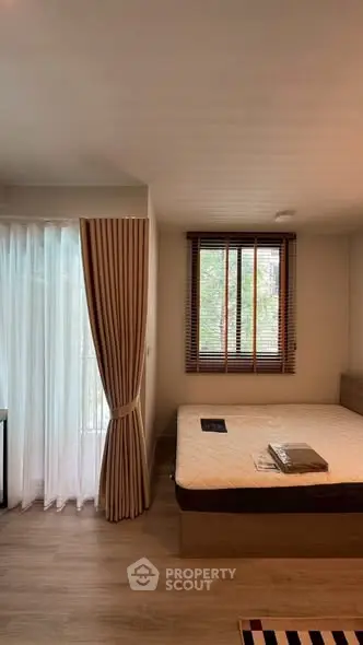 Cozy bedroom with large window and elegant curtains, featuring a comfortable bed and wooden flooring.