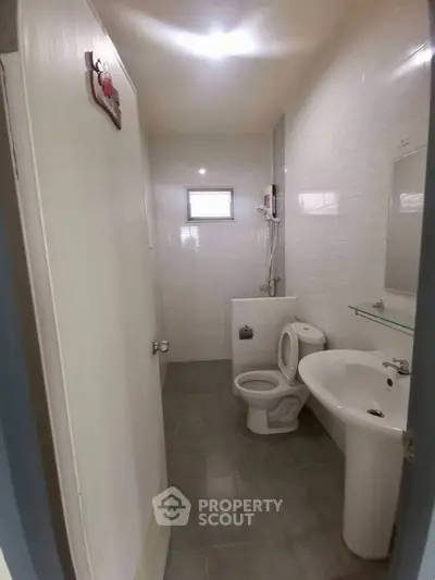 Compact bathroom with modern fixtures and tiled walls, featuring a toilet, sink, and shower area.
