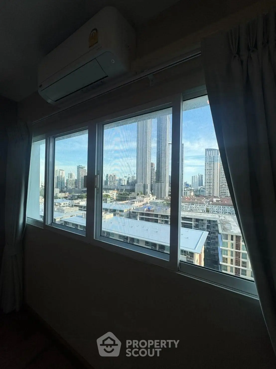Spacious room with large window offering stunning city skyline view, perfect for urban living.