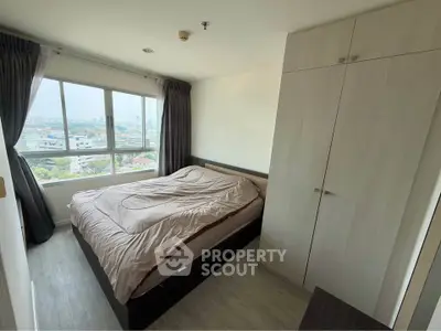 Cozy bedroom with large window offering stunning city views, featuring modern wardrobe and stylish decor.