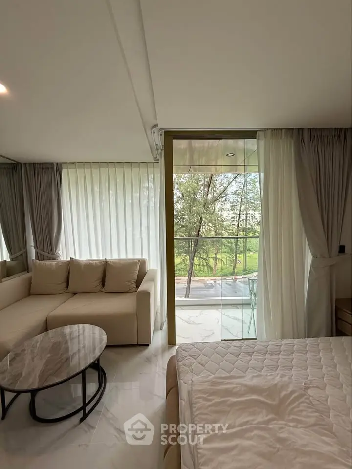 Modern living room with large windows and balcony overlooking greenery, featuring a cozy sofa and elegant decor.