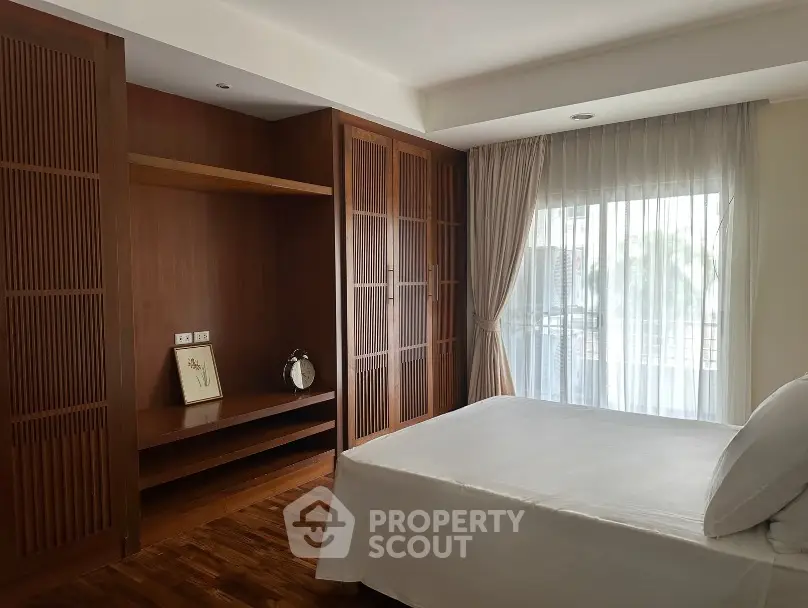 Spacious bedroom with wooden accents and large window offering natural light.