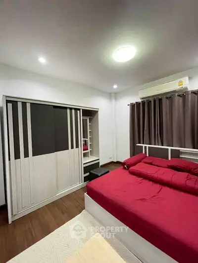 Modern bedroom with red bedding and sleek wardrobe in a cozy apartment.