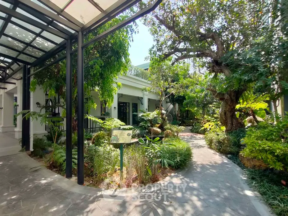 Lush garden entrance with mature trees and pathway leading to a charming house
