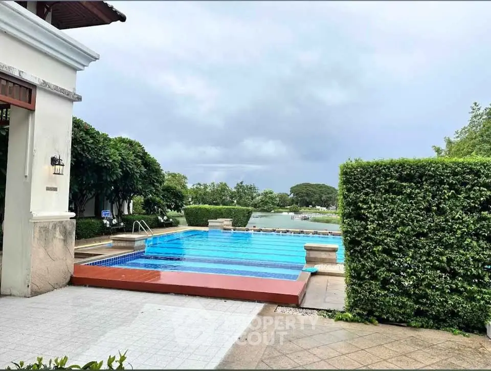 Luxurious outdoor pool area with lush greenery and serene water view, perfect for relaxation.