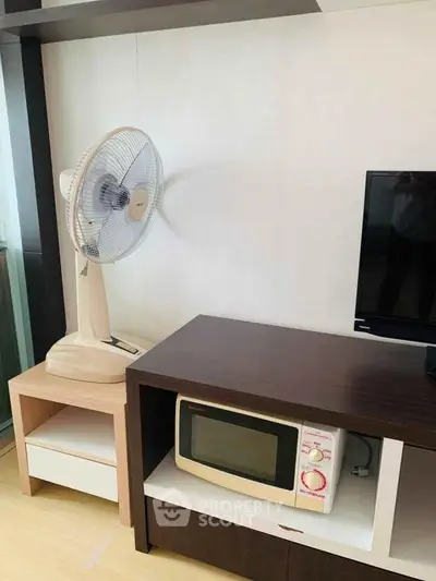 Modern living room corner with fan, microwave, and TV on stylish wooden furniture.