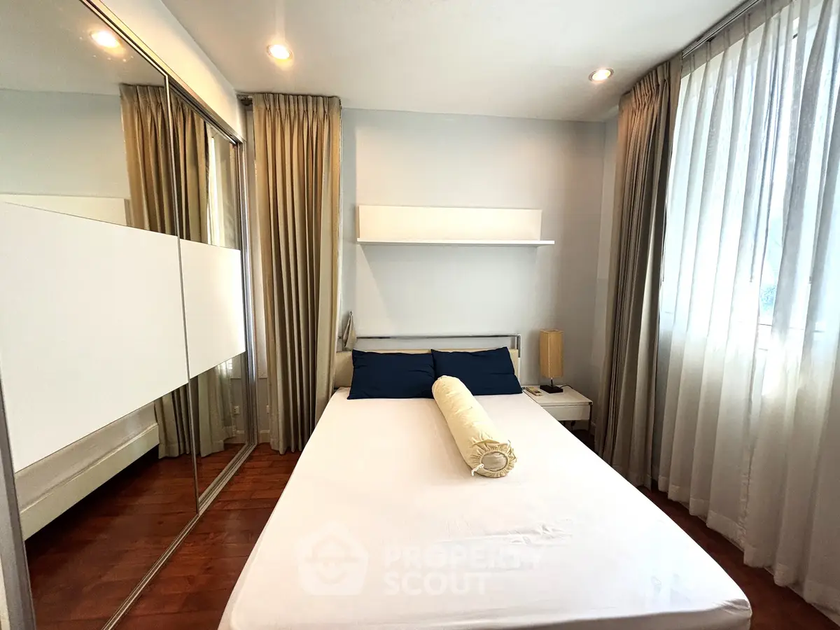 Cozy bedroom with large windows and mirrored closet doors, perfect for natural light lovers.