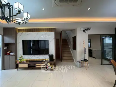 Modern living room with stylish decor and staircase, featuring a large TV and elegant lighting.