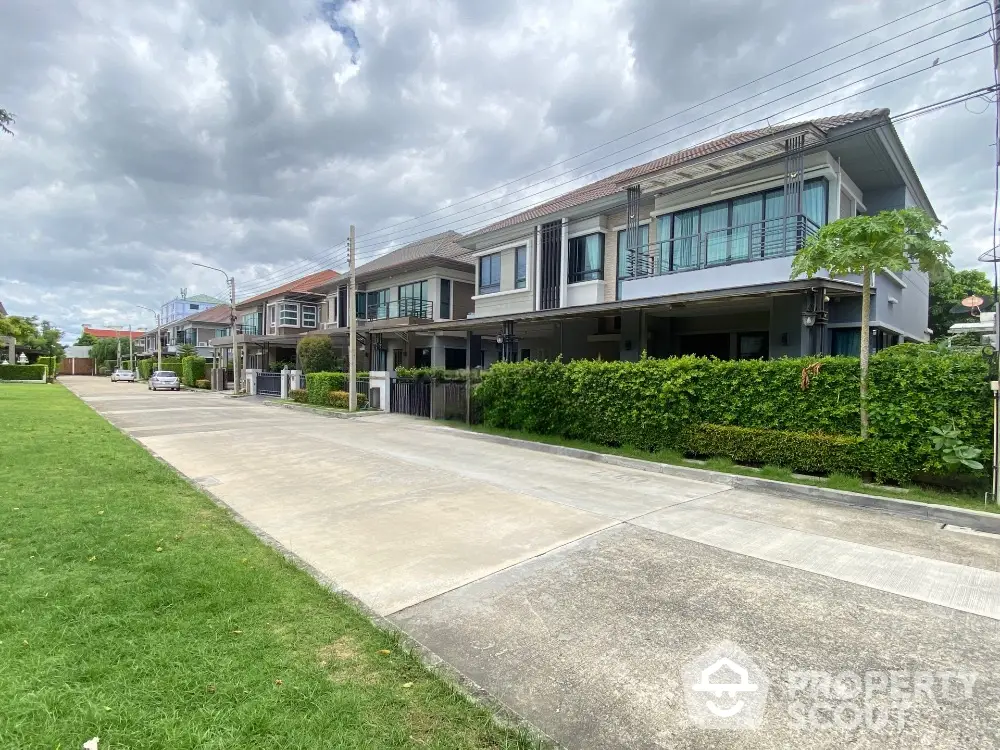 Modern suburban houses with lush greenery and spacious driveways under a cloudy sky.