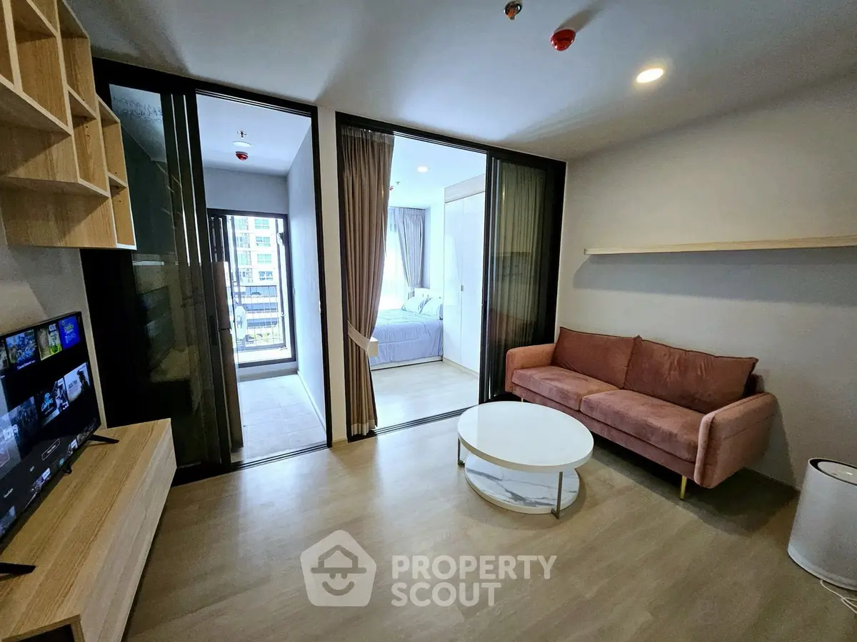 Modern living room with sliding doors leading to a cozy bedroom, featuring a stylish sofa and wall-mounted TV.