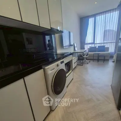 Modern living room with sleek kitchen appliances and large windows offering natural light.