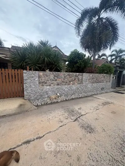 Charming residential property with stone wall and lush greenery in a tropical setting.