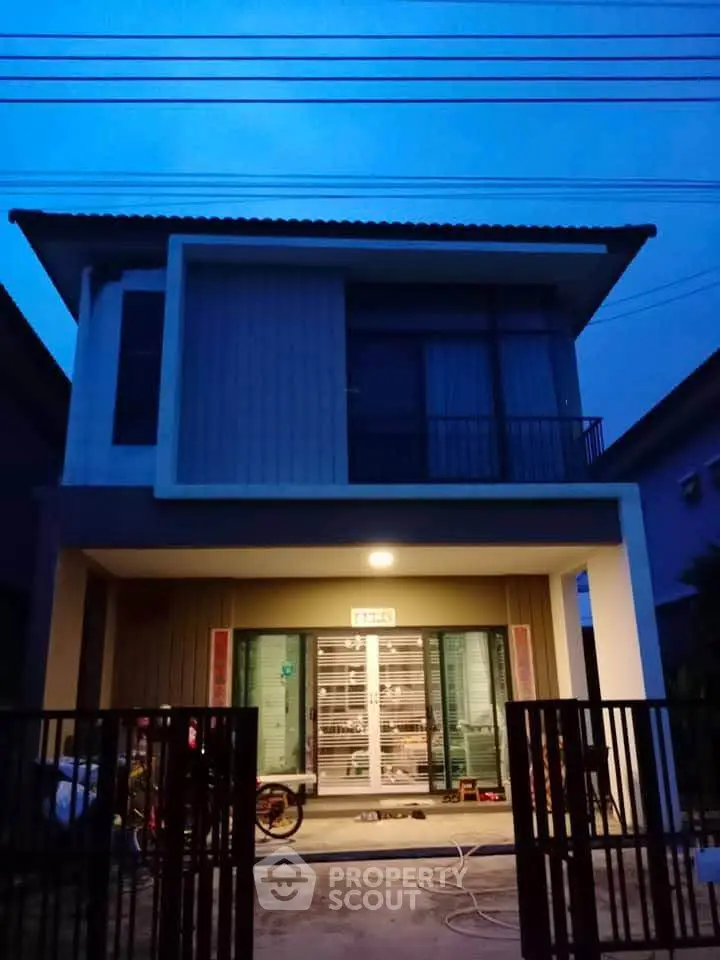 Modern two-story house with gated entrance and evening lighting
