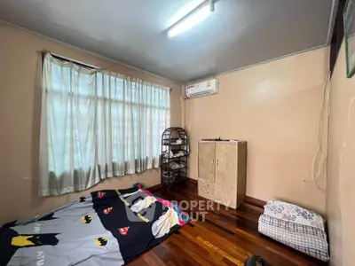 Cozy bedroom with wooden flooring and natural light, featuring air conditioning and simple furnishings.