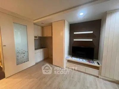 Modern living room with built-in TV unit and compact kitchen in open layout apartment.