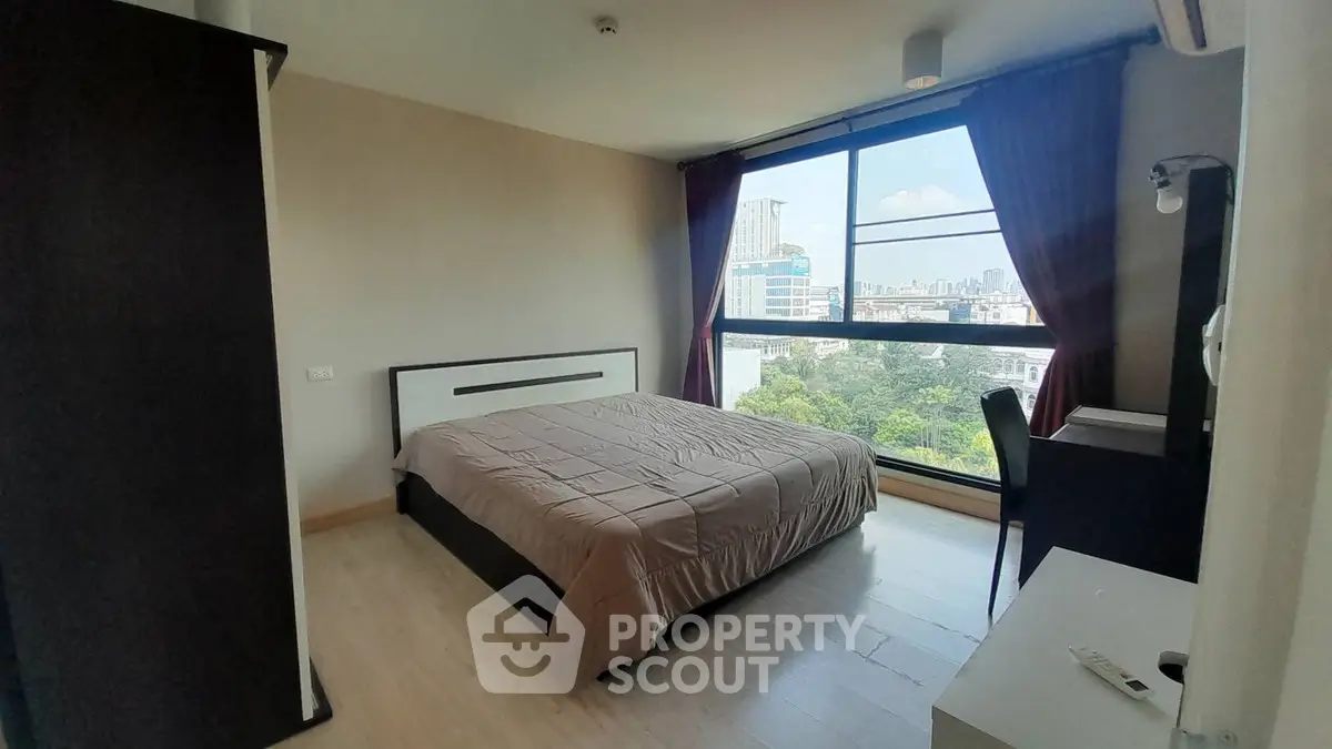 Spacious bedroom with large window offering stunning city views, modern furnishings, and ample natural light.