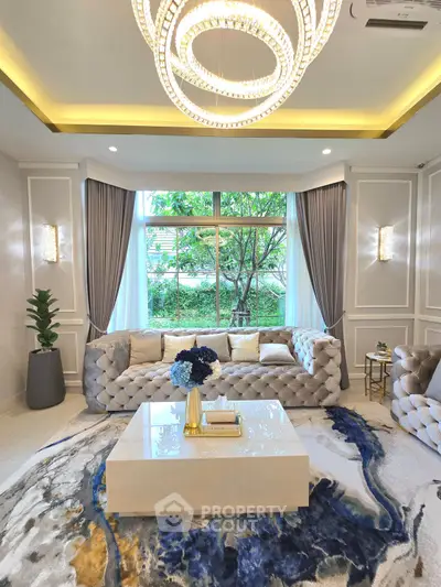 Luxurious living room with elegant chandelier and plush sofas, featuring large window with garden view.