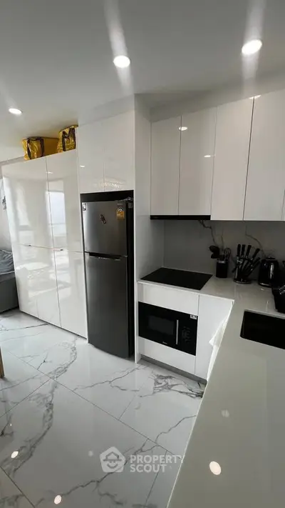 Modern kitchen with sleek white cabinets and marble flooring, featuring a fridge and built-in microwave.