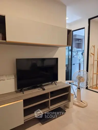 Modern living room with sleek TV stand and fan, open layout leading to kitchen area.