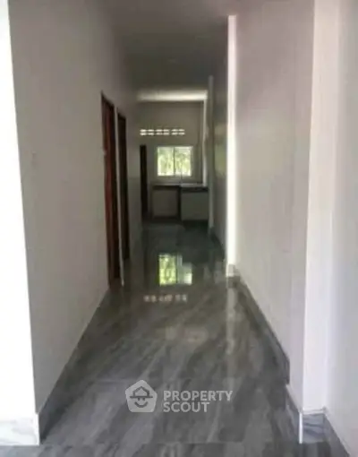 Spacious hallway with glossy tiled flooring leading to a bright room with large window.