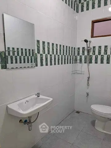 Modern bathroom with white tiles and green accents, featuring a shower and wall-mounted sink.
