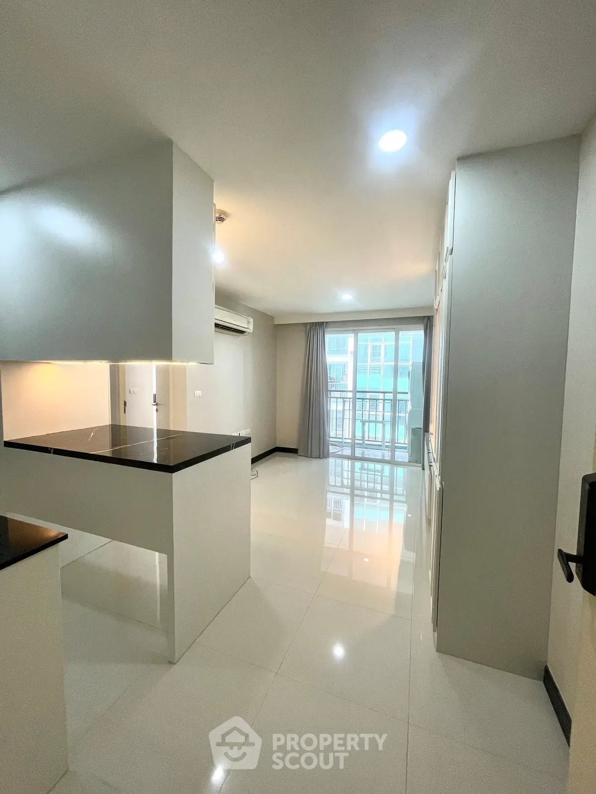 Modern open-layout kitchen with sleek countertops and bright living area leading to a balcony.