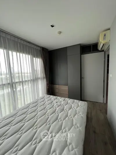 Modern bedroom with large window and built-in wardrobe, featuring sleek design and natural light.