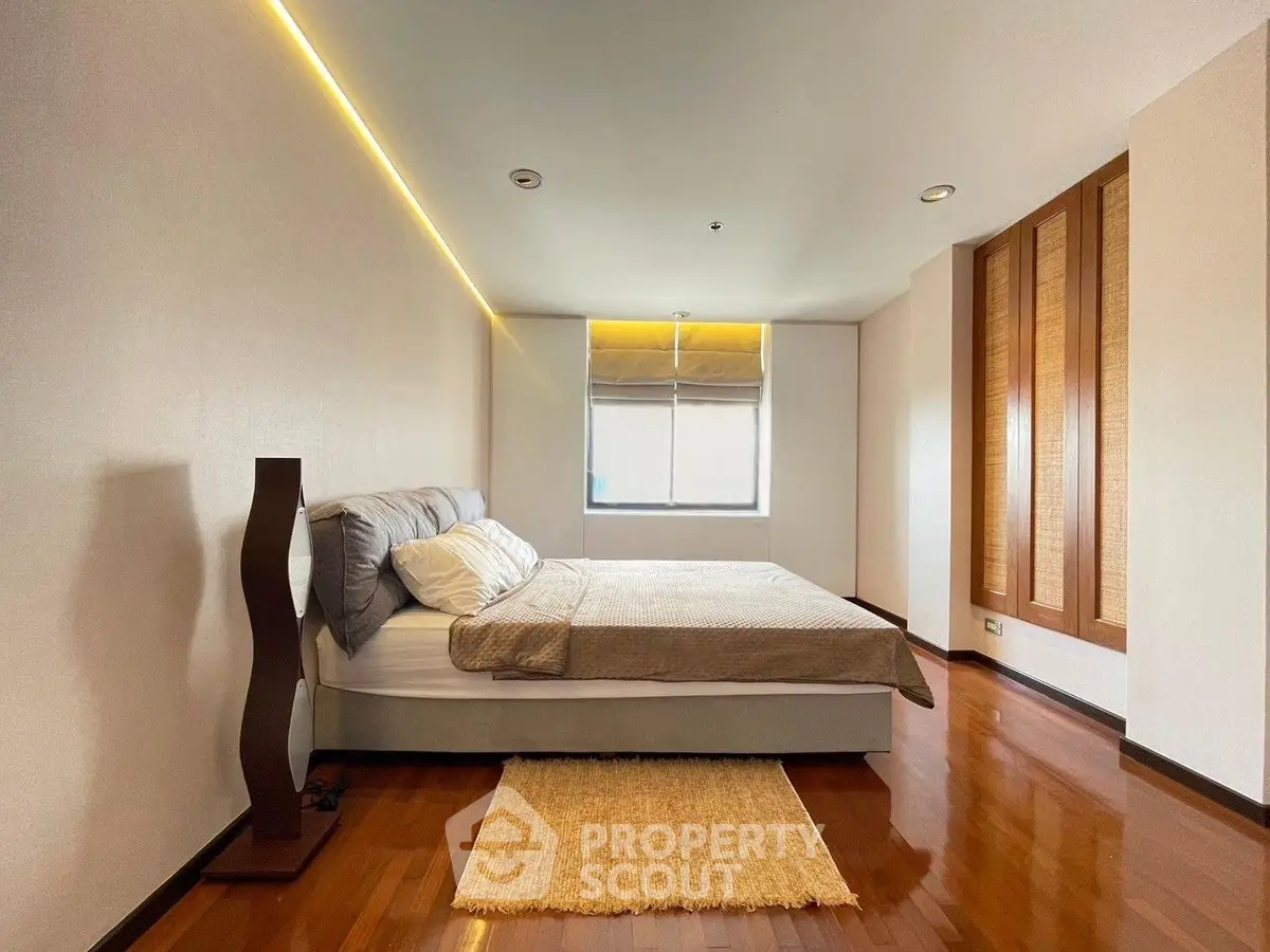 Spacious bedroom with modern design and wooden flooring, featuring a cozy bed and ambient lighting.